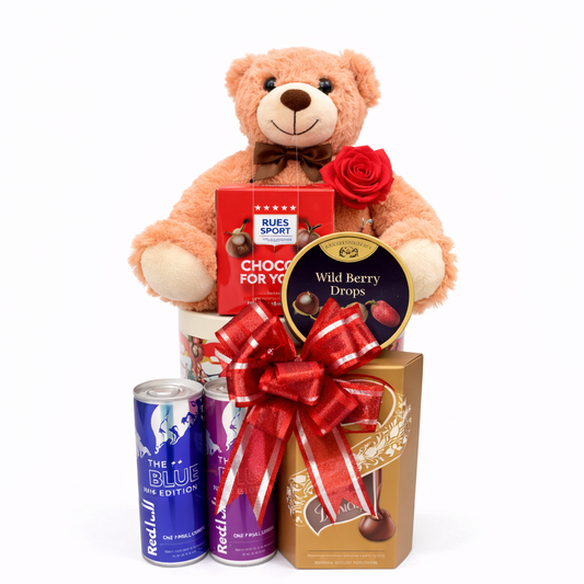 Teddy bear with gift basket including chocolates and drinks on a white background