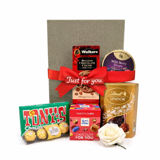 Assorted chocolate bars and a white rose in front of a gray gift box with a red ribbon.